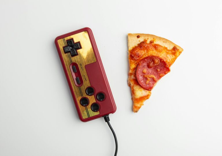 Top view of a retro gaming controller and a slice of pepperoni pizza on white background.